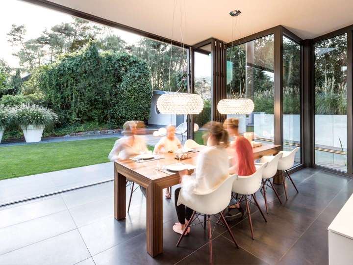 Familie sitz am Esstisch vor einer geöffneten Glas-Faltwand mit Blick in den Garten