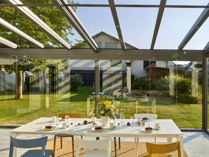 Innenansicht eines Glashauses mit Esstisch mit Blick in den grünen Garten